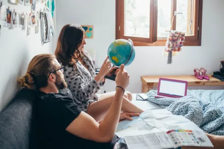 couple making travel plans in bed holding a globe 